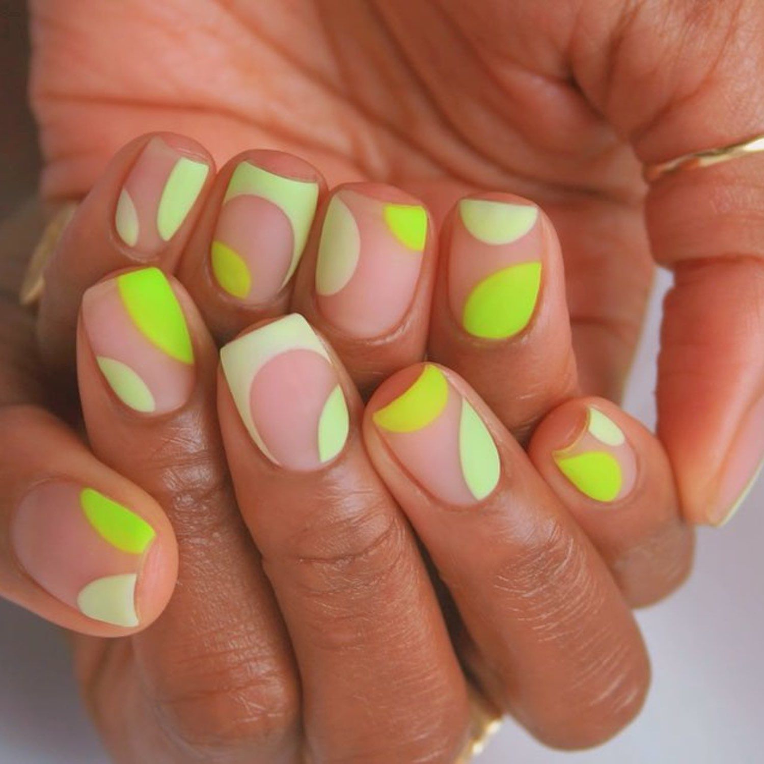 Manicure com uma base neutra e design abstrato amarelo e verde neon