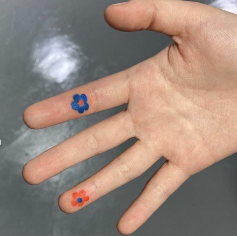 Tatuagens azuis e laranja na forma de pequenas cores nos dedos internos
