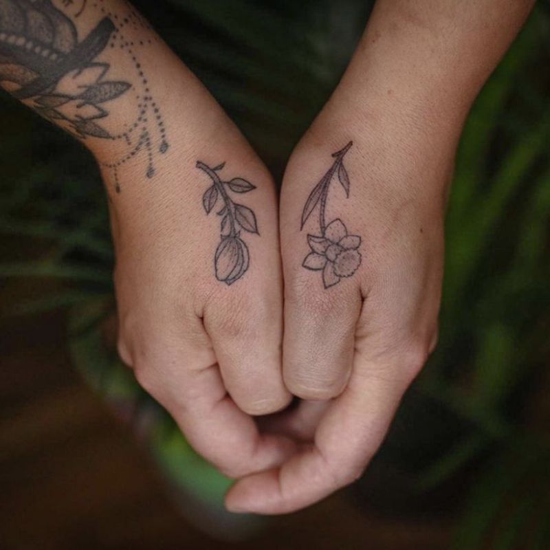 Duas tatuagens de flores diferentes na lateral dos polegares