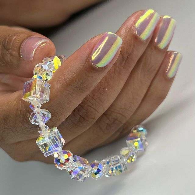Uma mão com uma manicure em gel de arc o-íris segura uma pulseira de cristais