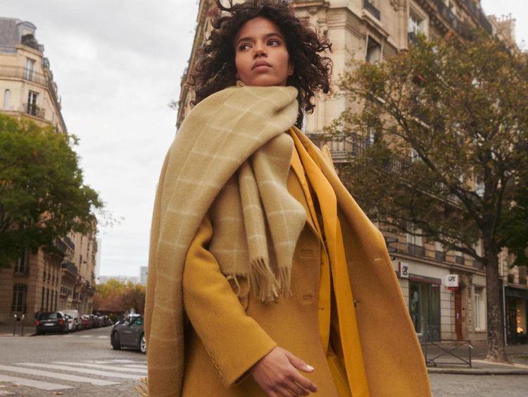 Uma mulher em um cachecol bege e um casaco amarelo em uma caminhada em Paris