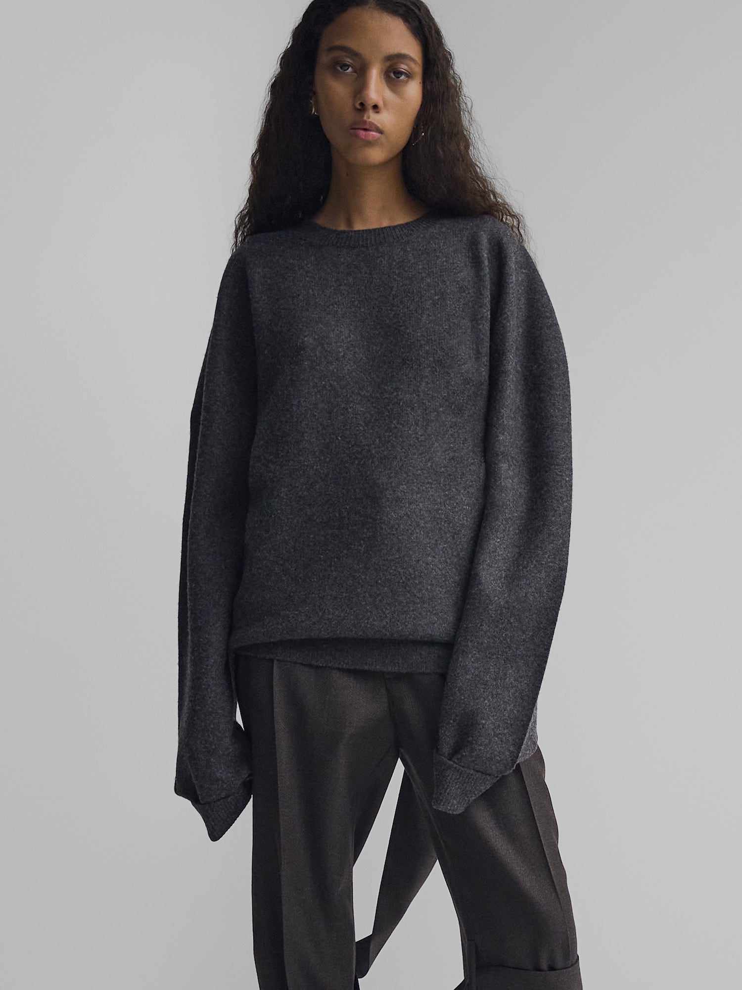 Modelo em um suéter de caxemira cinza-carbono com um decote redondo e calças plissadas de Phoebe Philo