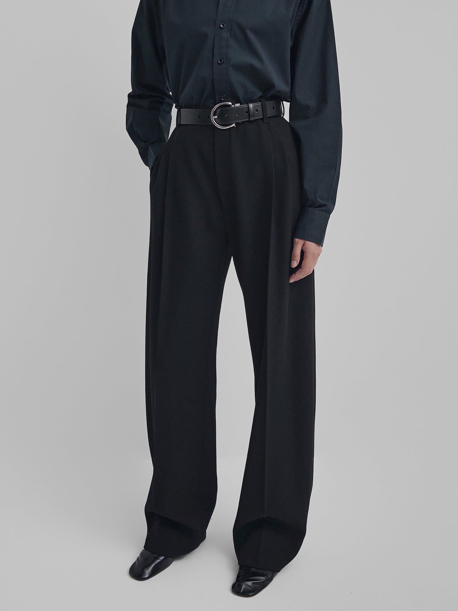 O modelo tem calças pretas, cinto, camisa de botão e sapatos com um dedo do pé quadrado de Phoebe Philo