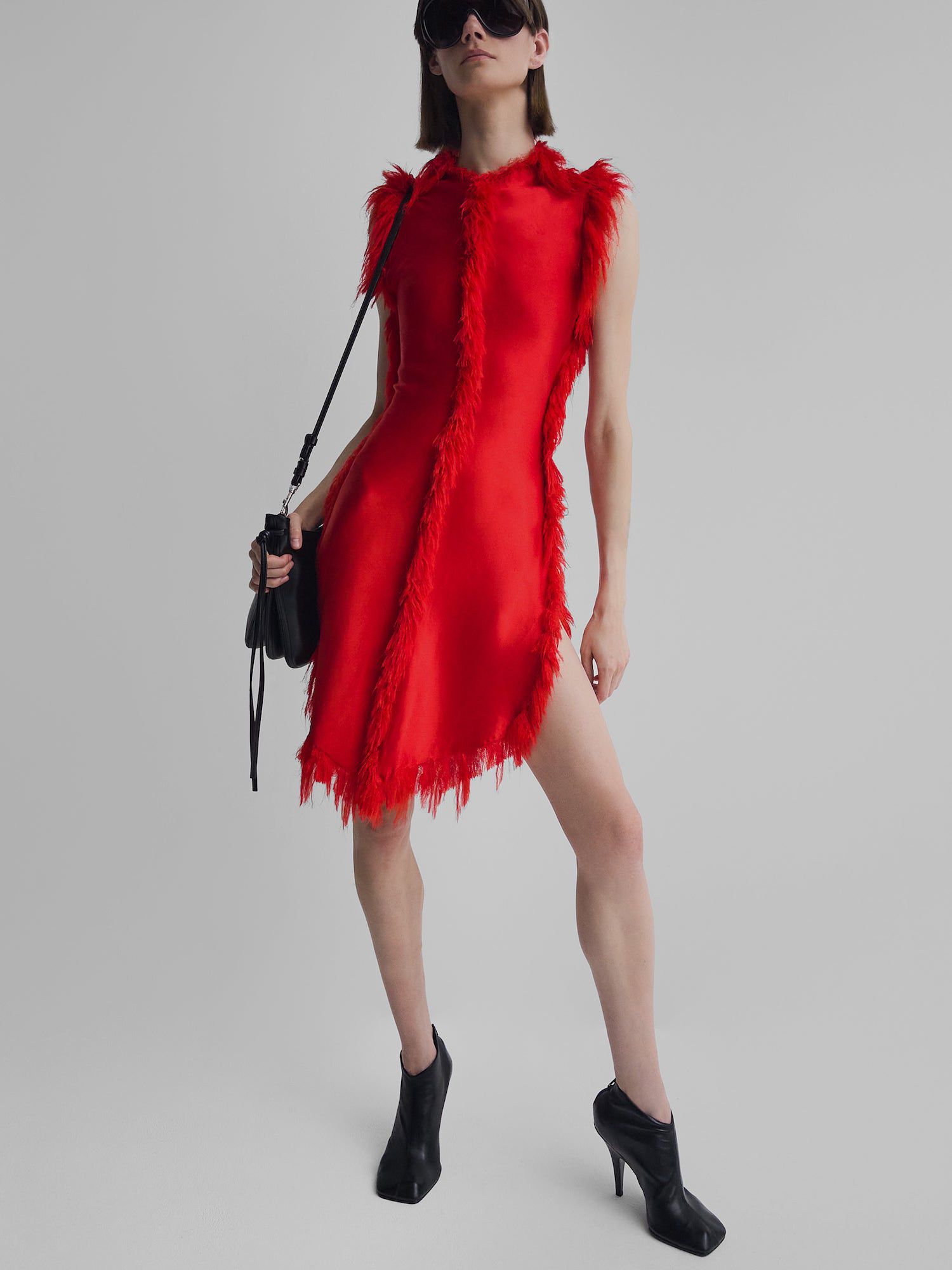 Modelo no mini-vestido vermelho Phoebe Philo com acabamento em bordados artesanais, emparelhado com botas de tornozelo preto, bolsa e óculos de sol
