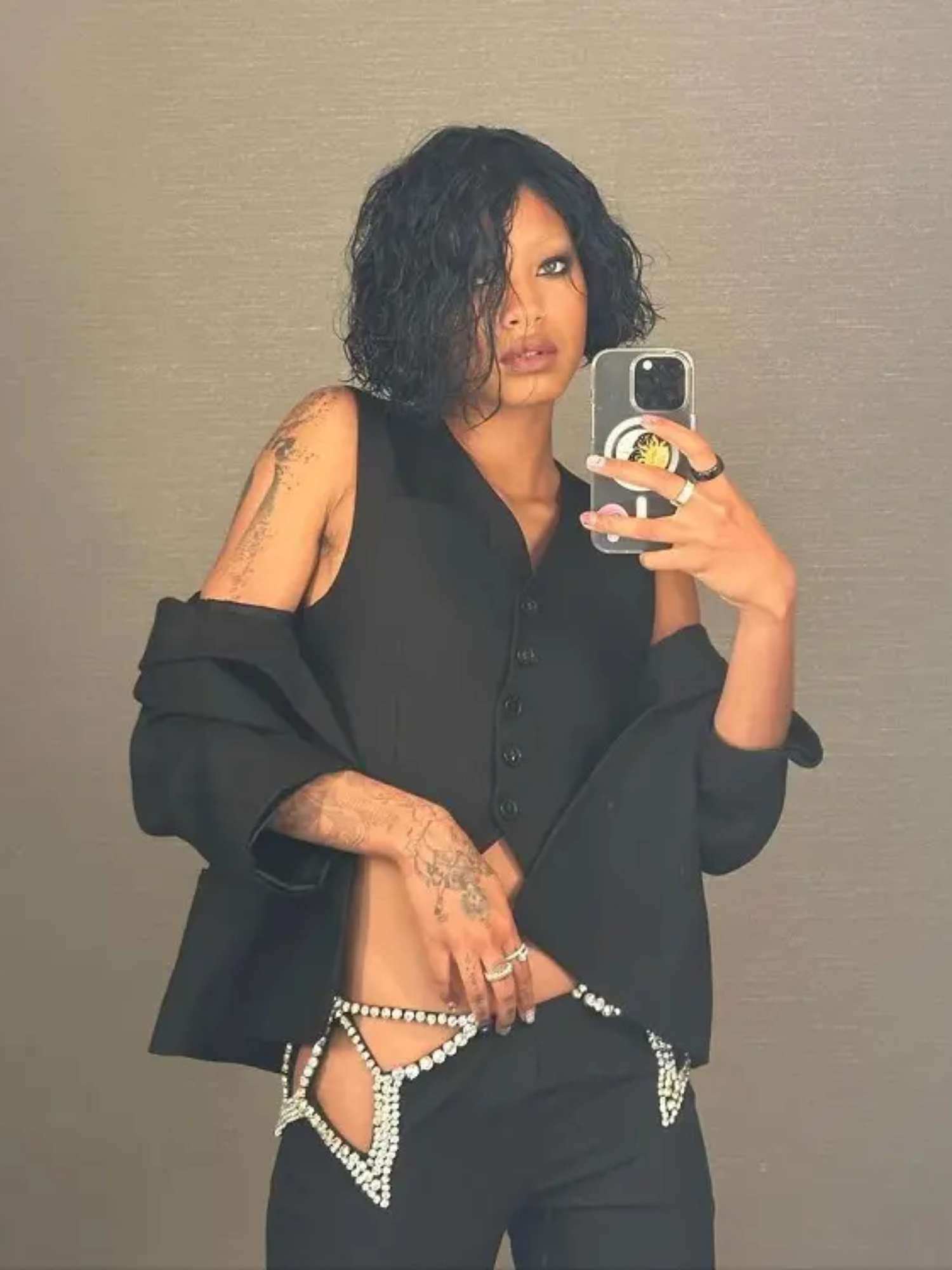 Willow Smith faz uma selfie espelho em um colete preto nos botões, uma jaqueta nas mãos, calças com cortes de strass prateados, anéis e maquiagem esfumaçada do olho