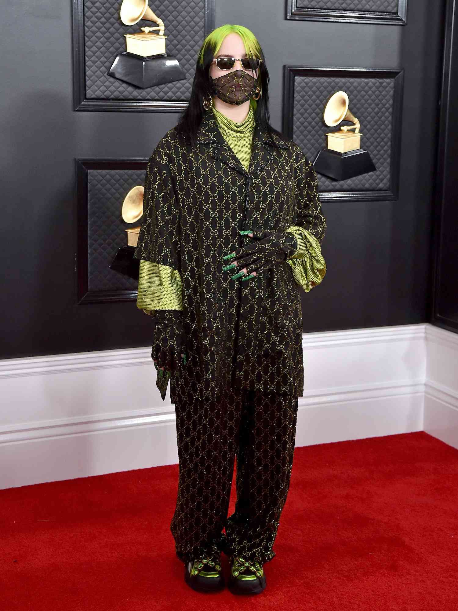 Billie Eilish em conjunto de calças com logotipo Gucci preto e verde, luvas sem dedos, tênis e máscara transparente