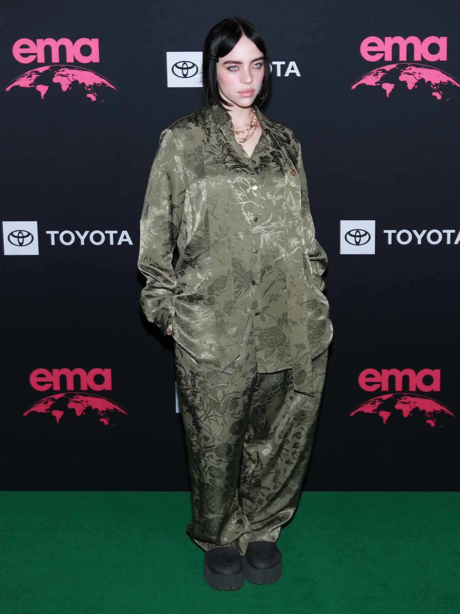 Billie Eilish usa pijama de seda Gucci floral verde, colar em camadas e botas pretas