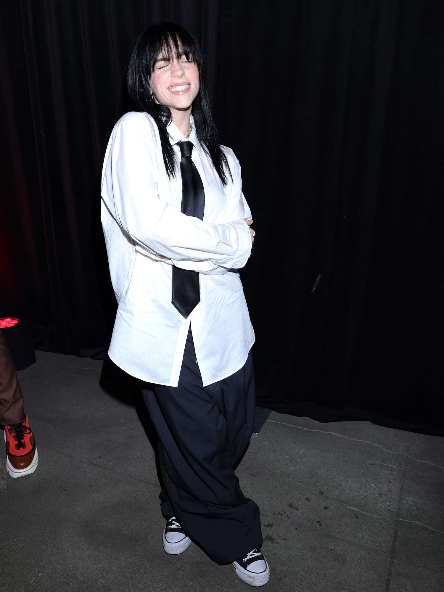 Billie Eilish usa camisa branca de botão, gravata preta e calça preta larga na estreia de The Swarm.
