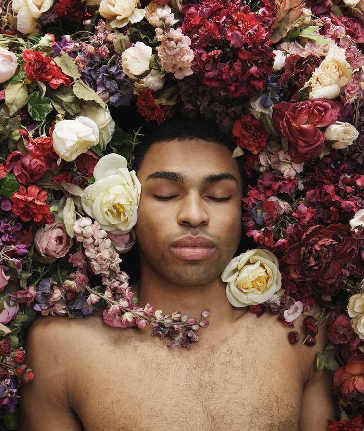 Jovem encontra-se em flores, olhos fechados, vista superior