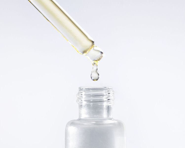 Um frasco transparente com uma pipeta de onde escorre óleo translúcido de cor quente.