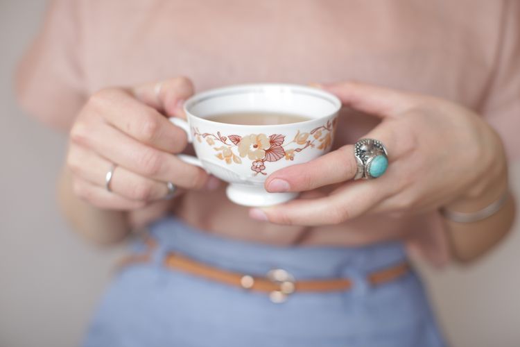Uma mulher em um anel azul segura uma xícara de chá