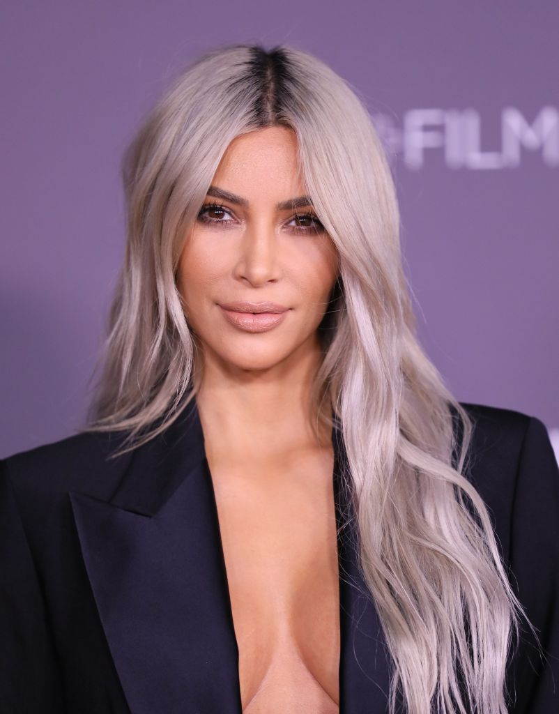 Kim Kardashian com cabelos grisalhos longos e ondulados com raízes escuras