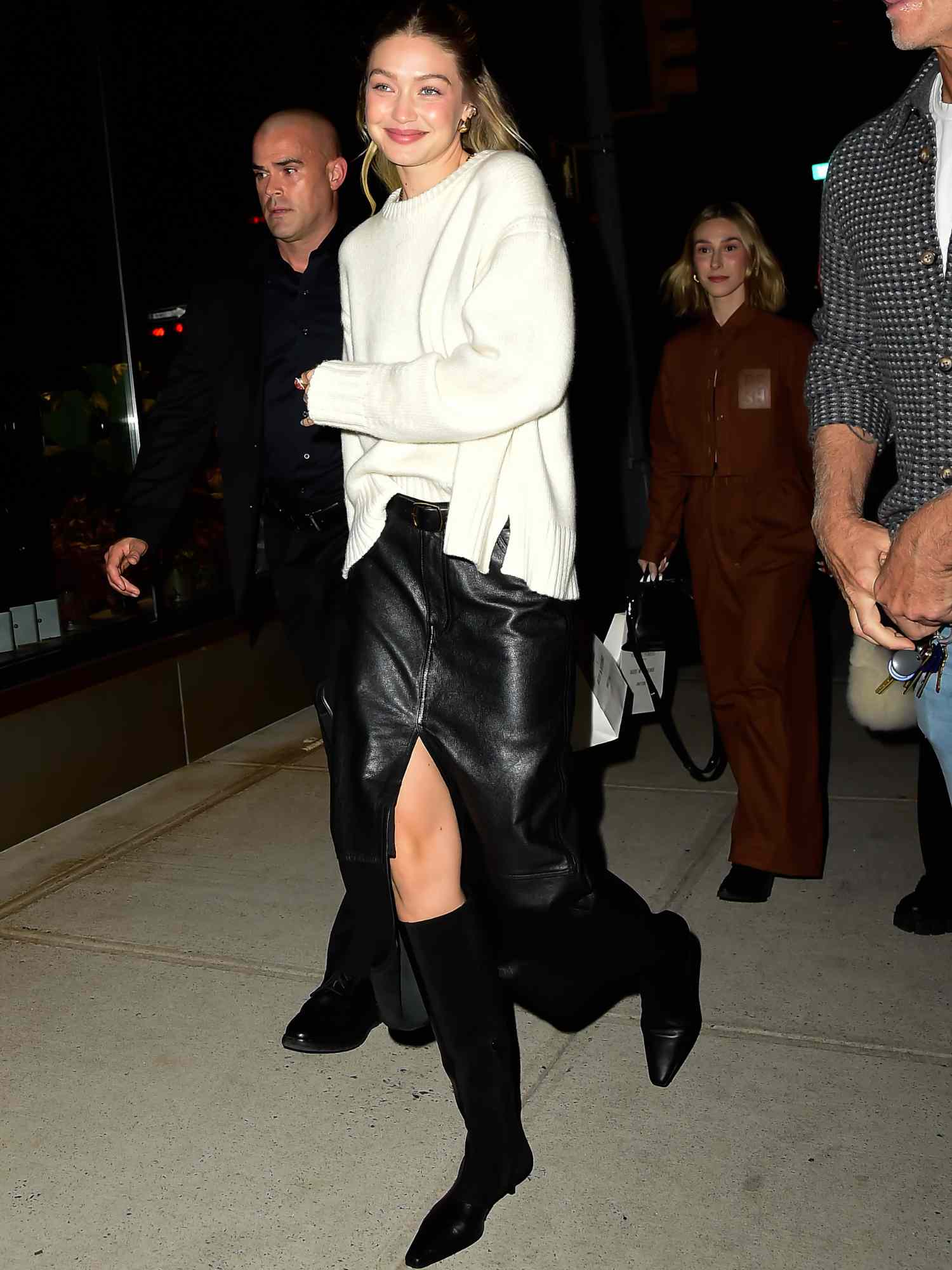 Gigi Hadid em saia midi de couro com fenda, suéter branco e botas de cano alto