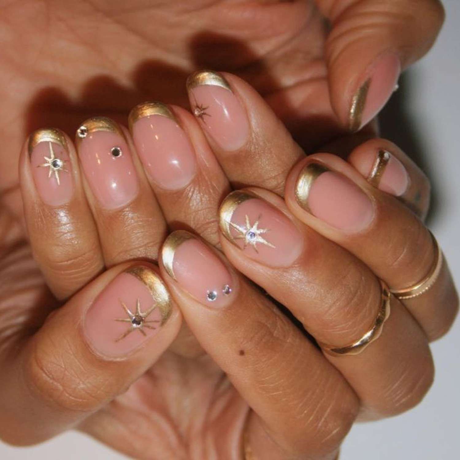 Manicure francesa com dicas de metal dourado, um padrão de estrelas e strass