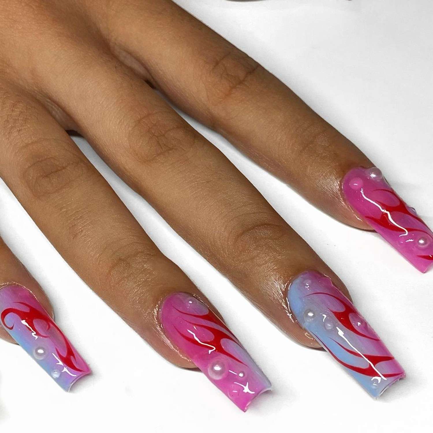 Mão com ombre de unhas rosa e rosa longas com um padrão vermelho e detalhes de pérola