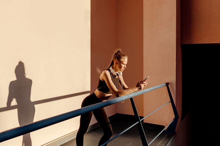 Uma mulher com equipamento de ginástica fica na varanda e olha para o telefone
