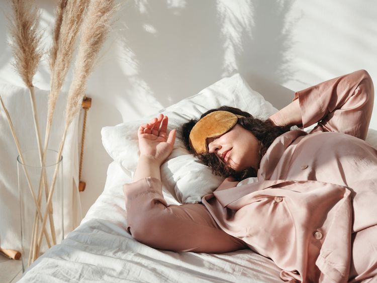 Uma mulher dorme em uma máscara para os olhos e pijamas nos botões na cama ao lado de um vaso com pampas