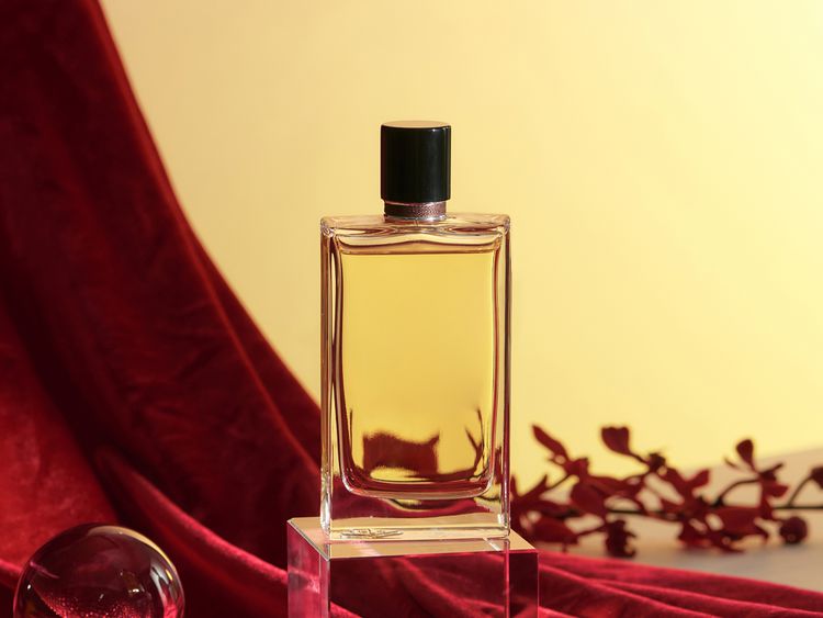 Garrafa de perfume na atmosfera de tons quentes com uma cortina vermelha e flores