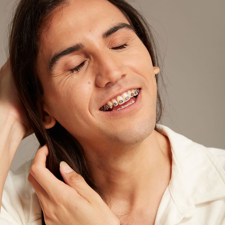 Um homem com olhos fechados e aparelho nos dentes, sorrindo