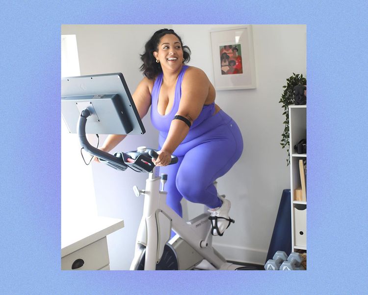 Uma mulher em roupas de fitness sorri em uma bicicleta estacionária.
