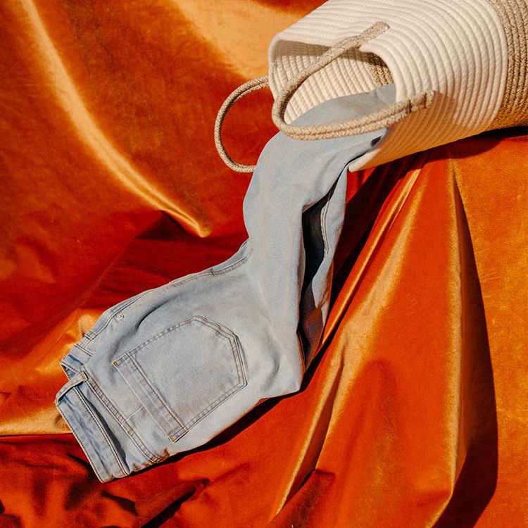 Um par de jeans caindo de uma bolsa e deitado em cima de um tecido laranja