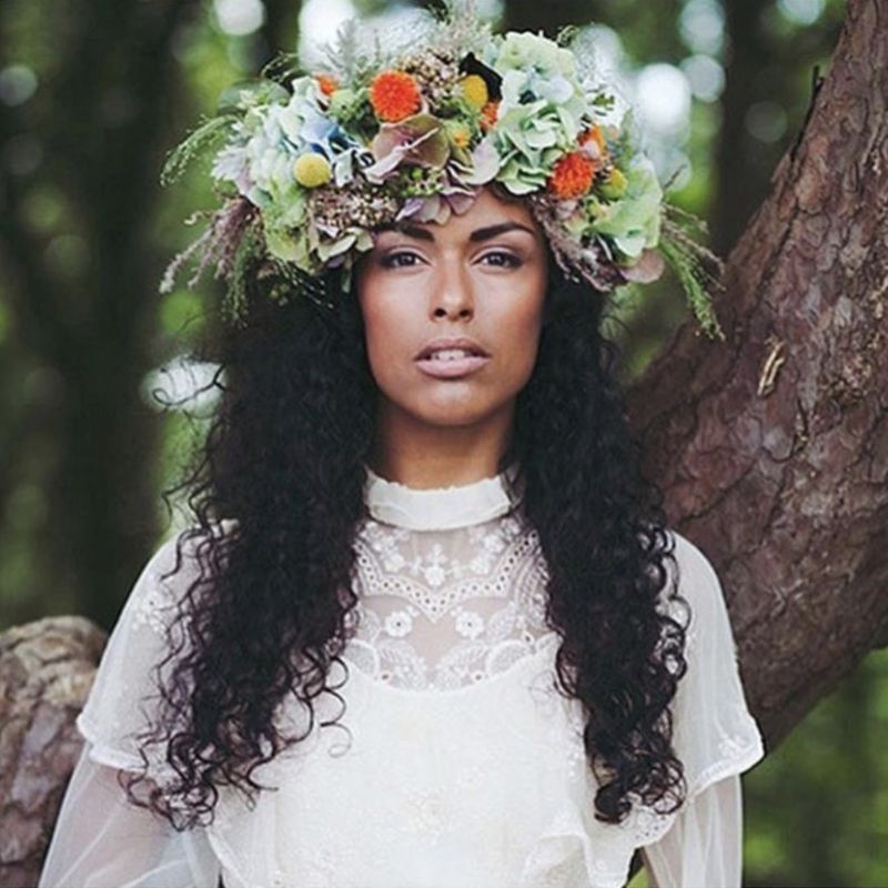A noiva usa cabelos cacheados longos com uma grande coroa de flores