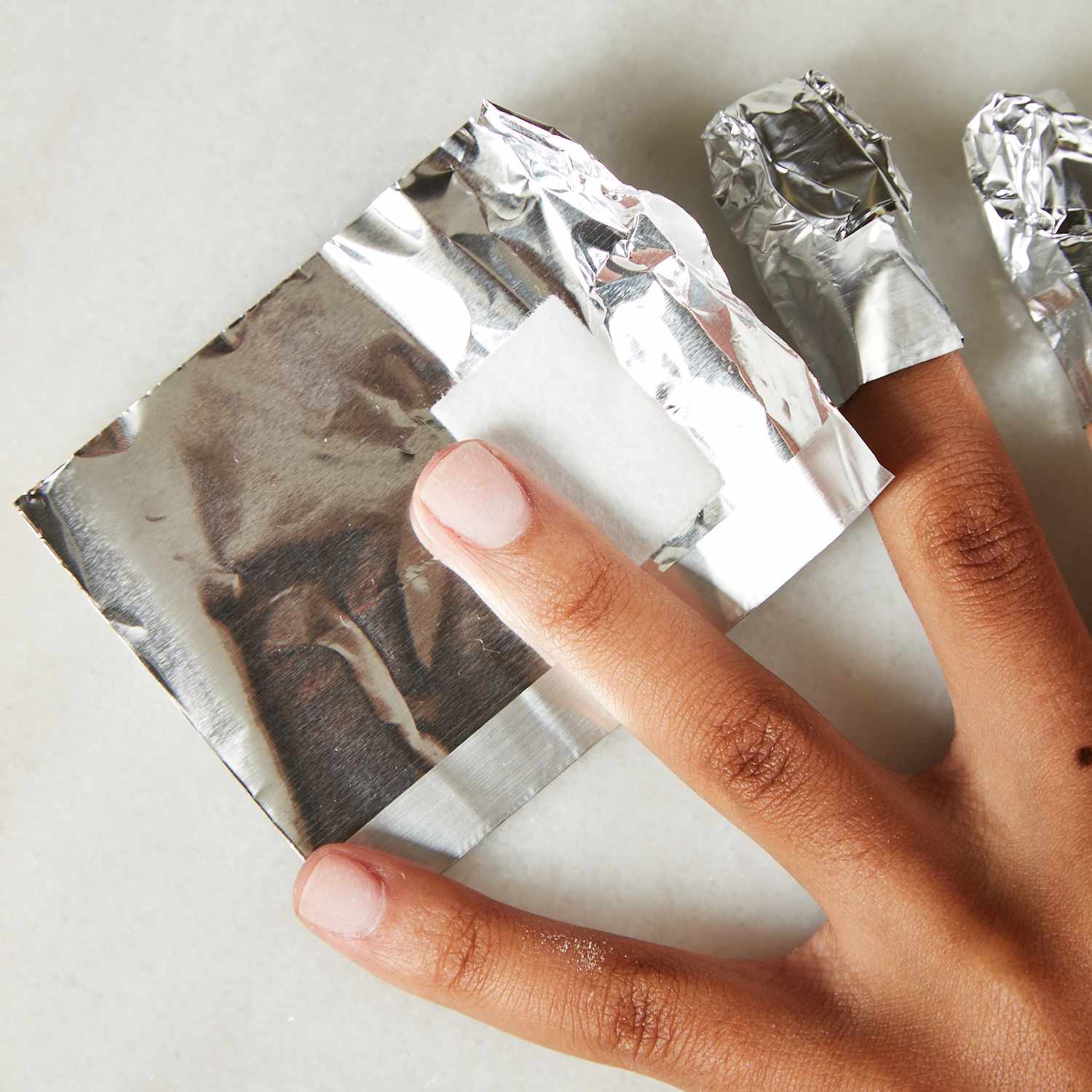 Uma mulher envolve o dedo em papel alumínio usando um pedaço de algodão embebido em acetona.
