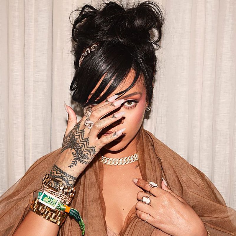 Rihanna cobre seu rosto para demonstrar uma tatuagem na mão feita por hena