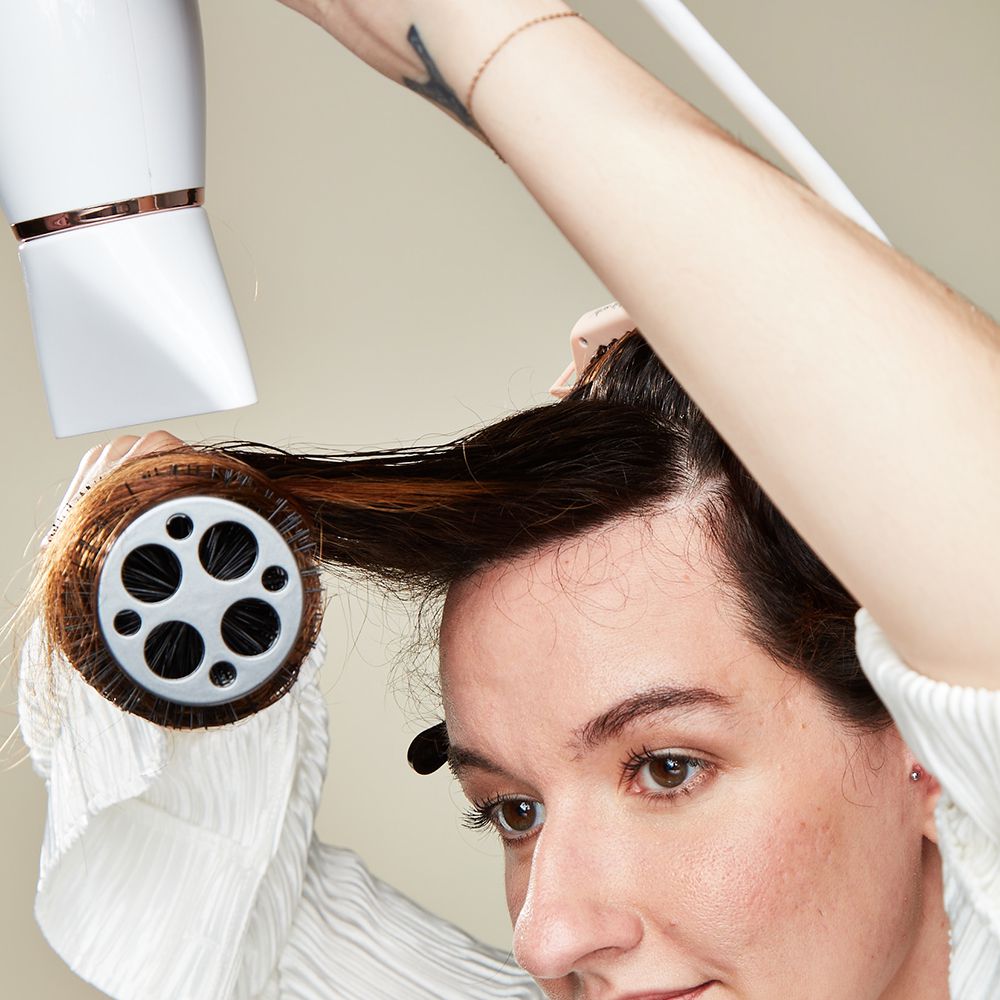 Modelo secando o cabelo com uma escova redonda