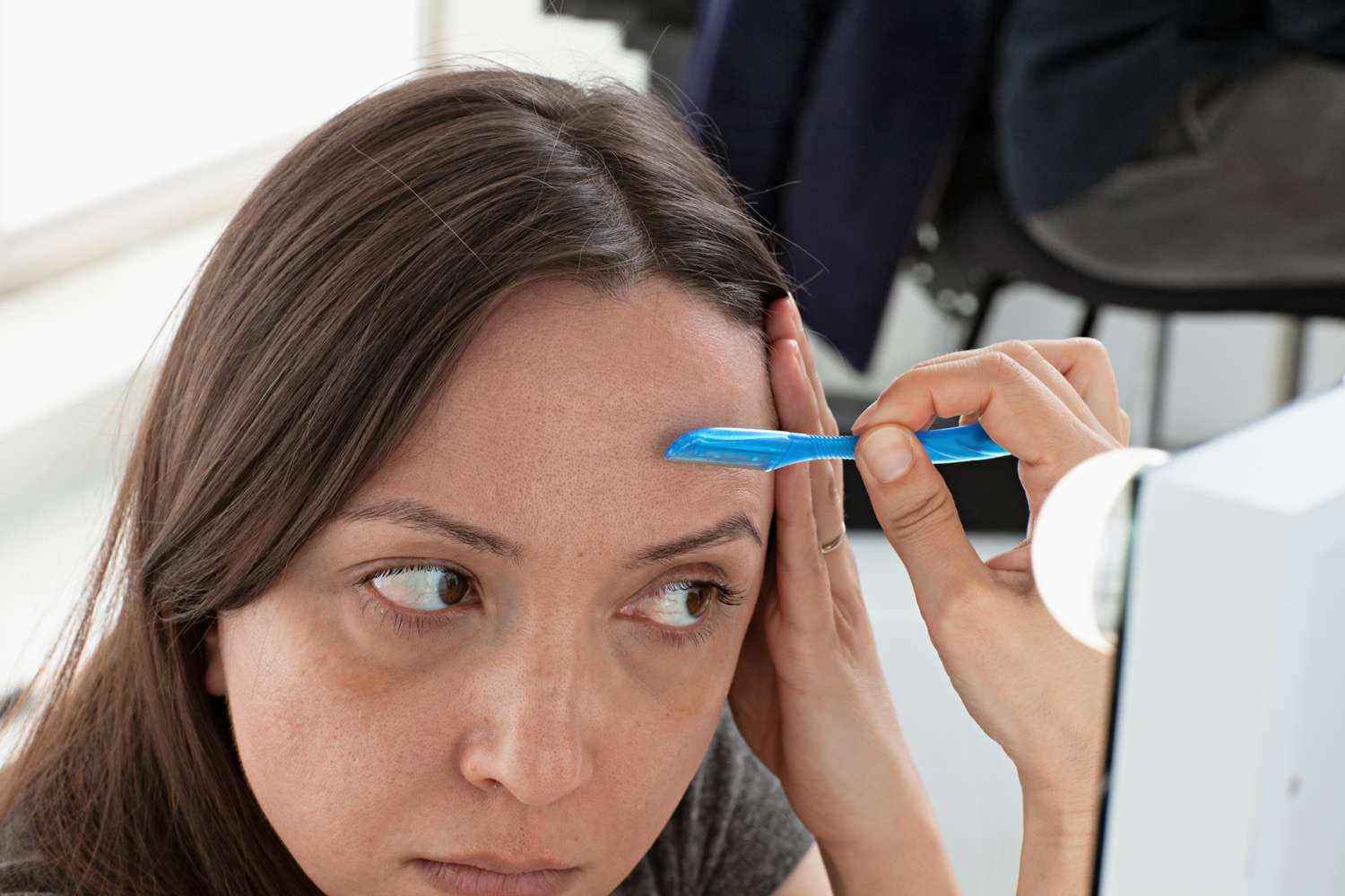 A mulher usa Schick Hydro Silk Touch-up esfoliando a ferramenta de dermaplaning na testa em frente ao espelho